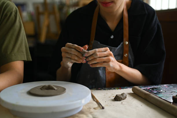 istock Craftspeople wearing aprons working with raw clay, shaping and decorating pottery in workshop. 1557653724