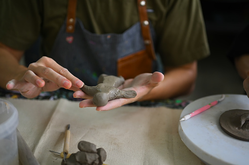 Image of young asian man enjoying creative process, creating handmade ceramics in pottery workshop.