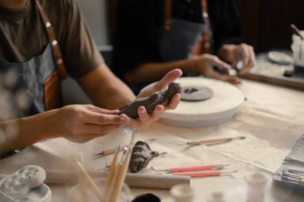 istock Craftspeople wearing aprons working with raw clay, shaping and decorating pottery in workshop. 1557654765