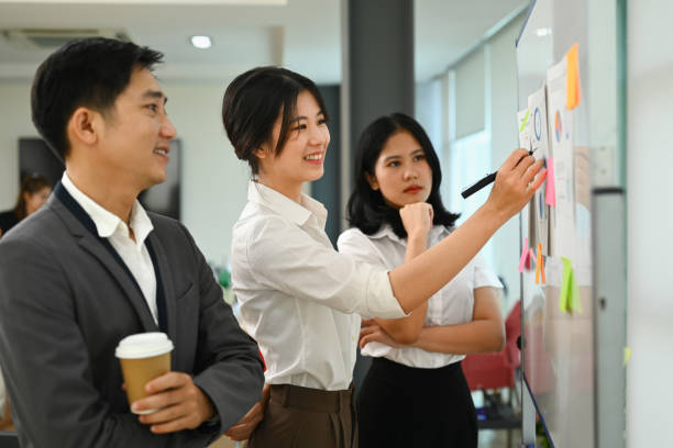 istock Professional female manager explaining project information on whiteboard during corporate meeting. 1557662398