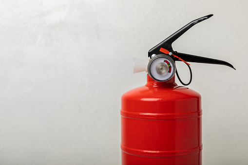 Fire extinguisher on the background of a black texture wall. Red fire extinguisher indoors on the wall. Fire protection, home fire extinguisher. Mockup, space for text, copy space.