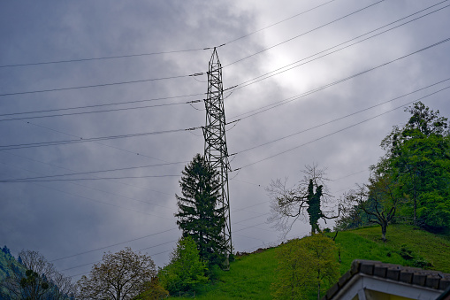 Looking up power line with pylons at Swiss village Sisikon on a cloudy spring day. Photo taken May 18th, 2023, Sisikon, Switzerland.
