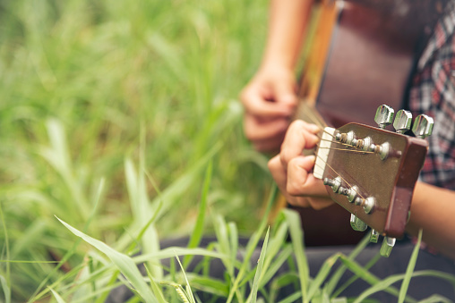 Young women playing acoustic guitar outdoor in green park. Woman person playing acoustic guitar music instrument at home, young Asian musician girl lifestyle in beautiful nature. Happy guitarist
