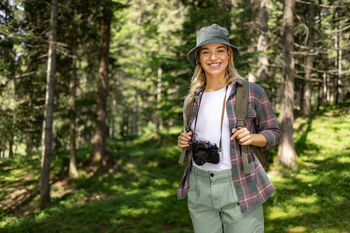 Happy female backpacker standing in the forest and looking at camera.