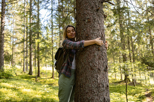 Young female tourist enjoying while embracing the tree in nature.
