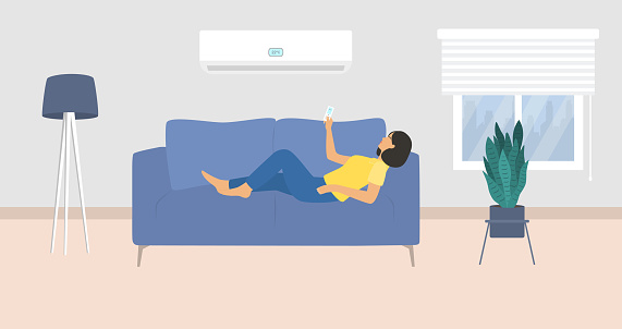 Young Woman Lying Down On Couch And Turning On Air Conditioner With Remote Controller