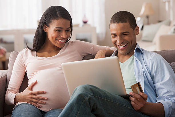młoda kobieta w ciąży siedzi z mężem dokonywania zakupów online - human pregnancy finance mixed race person holding zdjęcia i obrazy z banku zdjęć