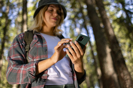 Close up of a female backpacker surfing the Internet on smart phone in the forest.