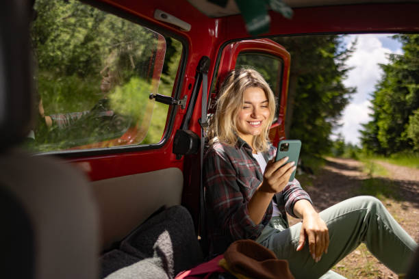 istock Happy woman text messaging on mobile phone while relaxing in her van. 1557738938