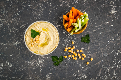 Bowl of hummus with carrot sticks and chickpeas, top view.