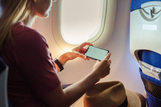 istock Young woman using smart phone in passenger airplane 1557797520