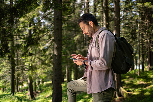 Young male tourist checking the map on his mobile phone in the woods.