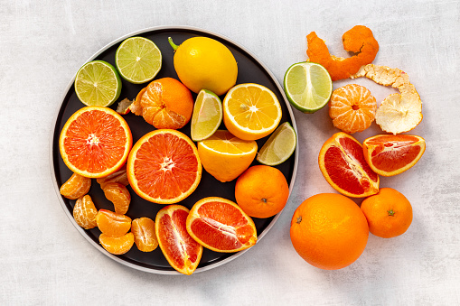 Citrus fruit on dark plate and black background, flat lat, from above.