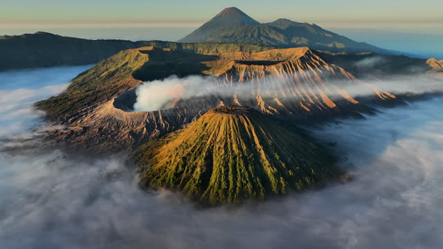 Aerial Drone Sunrise Scene of Eruption Volcano Mts. Bromo surrounded by Cloud, Fog and Smoke with mountain Semeru, Batok and Widodaren, Tengger Caldera,East Java, Java Island Indonesia
