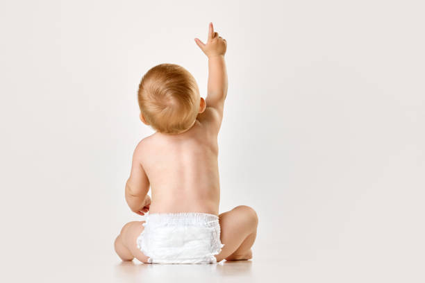 rückansicht des kleinen babys, kindes, kleinkindes, das in der windel vor weißem studiohintergrund sitzt. neugieriges baby - windel stock-fotos und bilder