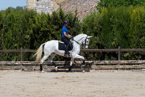 In an equestrian training center a young jockey rides a beautiful white mare. Equestrian training at a dressage and riding center. Exercise in free time.