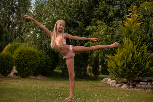 A little girl is professionally engaged in gymnastics and shows her skills in the summer on the street