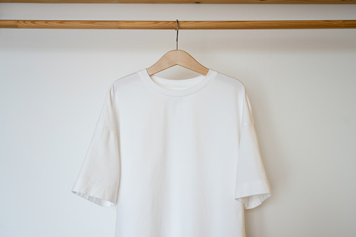 White t-shirt hanging on wooden hanger in white room.