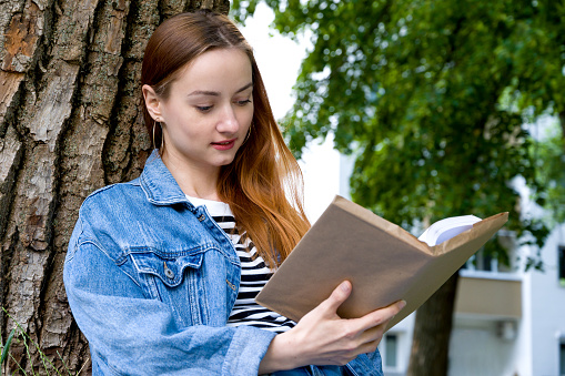 Portrait of happy student reading book outside. Education concept