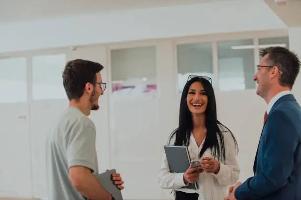 Photo of The director conducts a conversation with the secretary and a young programmer in a modern and spacious corridor of a large company, discussing various business topics and projects.