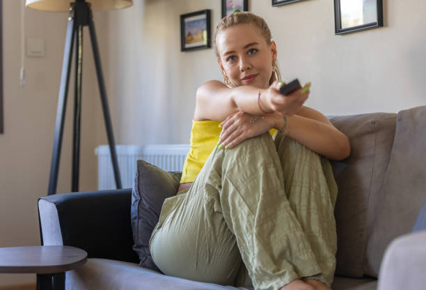 istock Pretty young woman is watching television on sofa. 1557883793