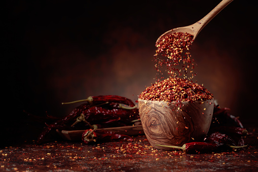 Chilli flakes are poured into a wooden dish. Chilli flakes and dried chili peppers on a brown background. Copy space.