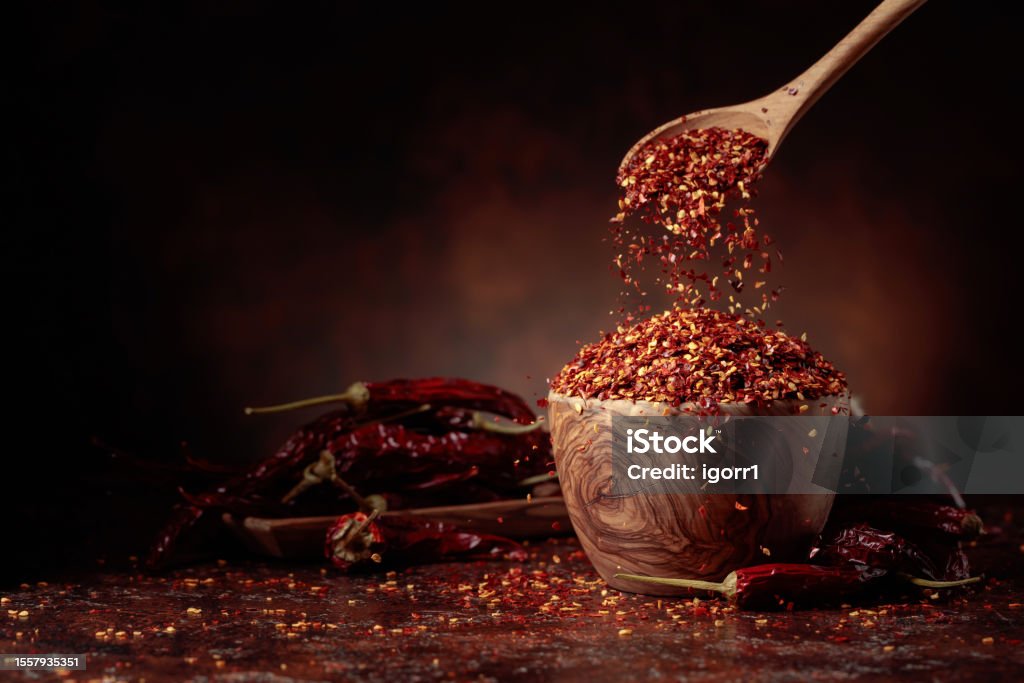 Chilli flakes are poured into a wooden dish. Chilli flakes are poured into a wooden dish. Chilli flakes and dried chili peppers on a brown background. Copy space. Herbal Medicine Stock Photo