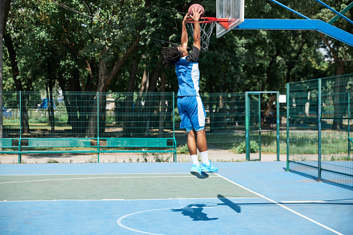 Full-length image of young man, sportsman playing basketball on warm sunny day. Outdoor sportsground. Concept of professional sport, competition, hobby, game, active lifestyle