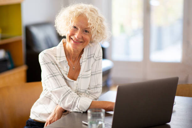 istock smiling older woman sitting at home with laptop computer looking at camera 1557948435