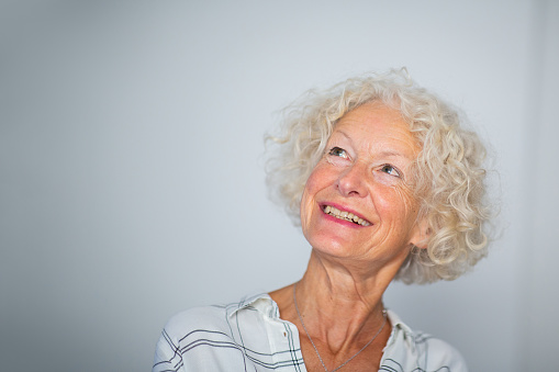 Close up portrait smiling older woman against gray background looking away