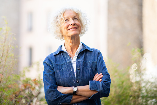 Portrait older woman posing with arms crossed outside and looking away