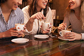 Group of three unrecognizable girl friends drinking coffee sitting in a table of a cafe.