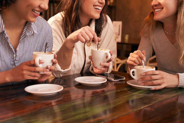 Group of three unrecognizable girl friends drinking coffee sitting in a table of a cafe. stock photo