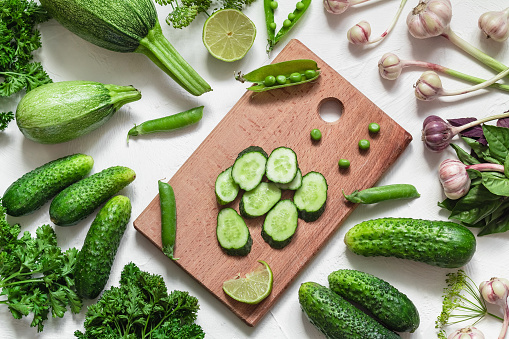Organic green vegatables and cutting board on a white background. Cucumbers, garlic, green pea, parsley, basil, zucchini.