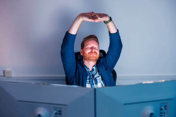 Tired businessman stretching at his desk while working late at the office