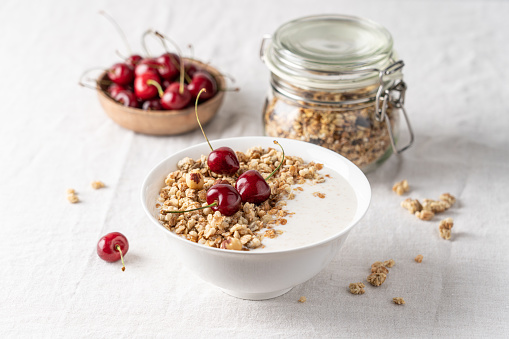 healthy granola breakfast with nuts and cherry in white bowl on light background