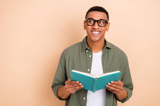 istock Photo of funky dreamy guy dressed khaki shirt spectacles enjoying novel looking empty space isolated beige color background 1557981663