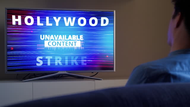 Back view of man upset reaction on Hollywood Strike 2023 Warning on TV screen