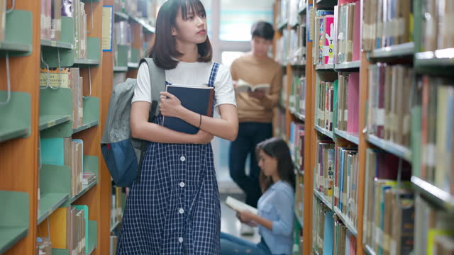 University student woman walking and searching the book on bookshelf in library at university