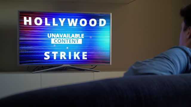 Man sits in front of TV and turns on news about Hollywood Strike 2023