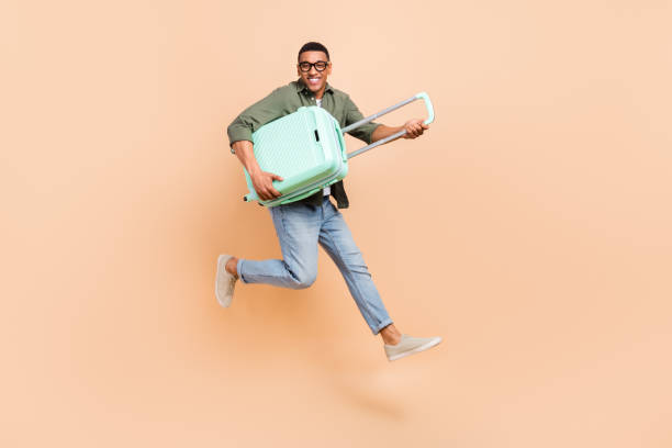 istock Full size profile portrait of excited cheerful man jumping hands hold suitcase empty space isolated on beige color background 1558023056