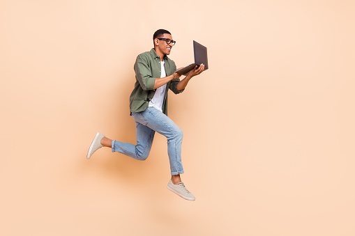 Full size profile photo of crazy active guy jump rush use netbook empty space isolated on beige color background.