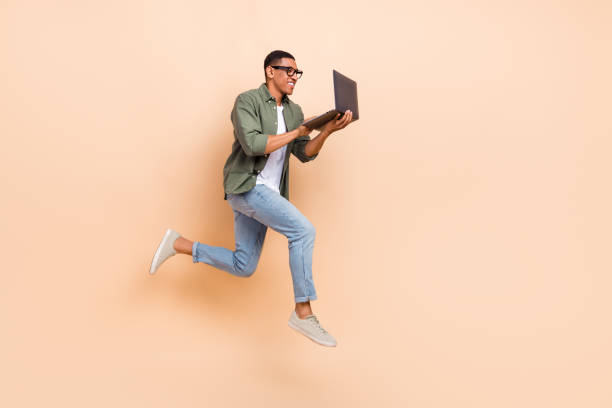Full size profile photo of crazy active guy jump rush use netbook empty space isolated on beige color background stock photo
