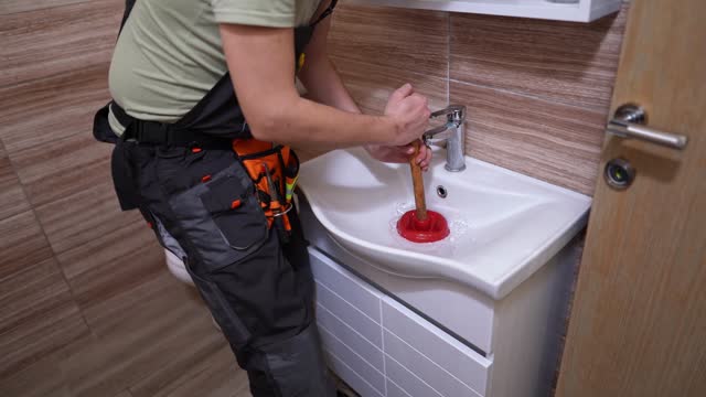 Mid adult male plumber unclogging bathroom sink