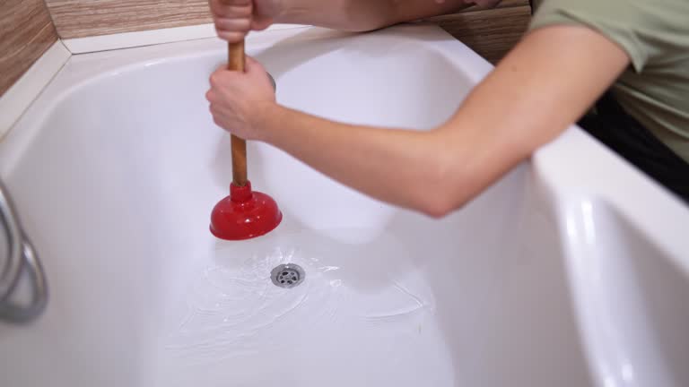 Mid adult male plumber unclogging bathtub drain