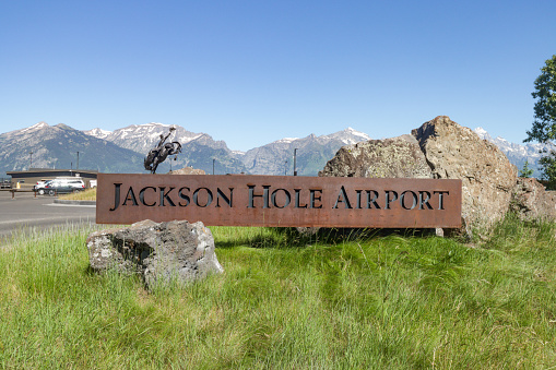 The welcome sign for Jackson Hole Airport in Teton County, Wyoming. BEHIND the place sign a 4,000 pound sculpture of a cowboy in a rodeo known as 'Battle of Wills', as designed by Bart Walter in 2016 to welcome visitors to the Cowboy State. The sign and the statue are two separate structures. This airport, a national monument, is the only US airport to be located in a national park - Grand Teton National Park in this case.