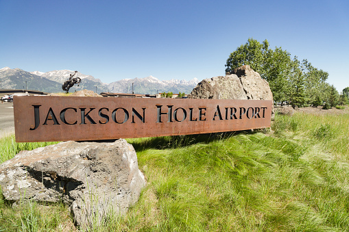 The welcome sign for Jackson Hole Airport in Teton County, Wyoming. BEHIND the place sign is a 4,000 pound sculpture of a cowboy in a rodeo known as 'Battle of Wills', as designed by Bart Walter in 2016 to welcome visitors to the Cowboy State. The sign and the statue are two separate structures. This airport, a national monument, is the only US airport to be located in a national park - Grand Teton National Park in this case.