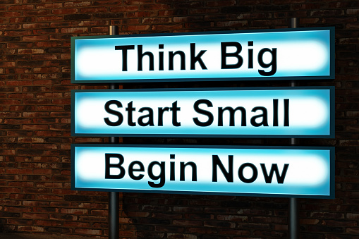 Think Big, start small, begin now. Black letters on a blue illumintaed light box, red brick wall. Thinking, ideas, beinnings. small business, strategy, motivation, encouragement. 3D illustration