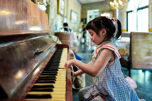 Asian little girl play piano in restaurant ,she concentrate put her finger on old classic piano so funny.