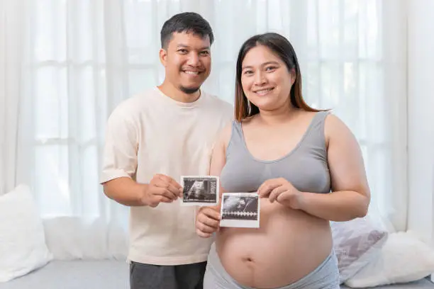 Asian pregnant woman with Thai husband at home. Love couple together and unborn baby. Family lifestyle.